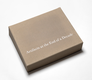 Tan cloth box against a white backdrop. White serif font on top of the box reads "Artifacts at the End of a Decade".