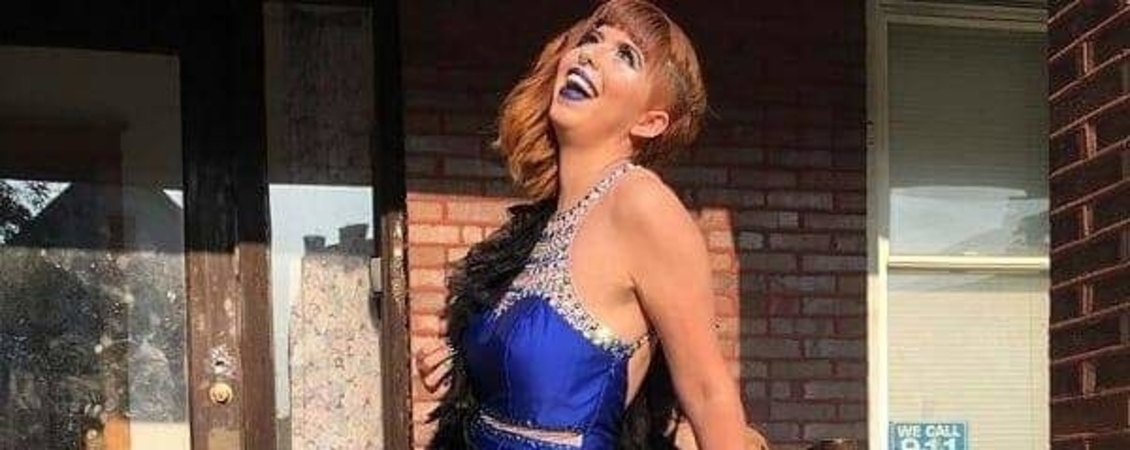 Photo of Gigi Bella. She is wearing a dark blue dress with a rhinestone neckline. She is throwing her head back and smiling widely.