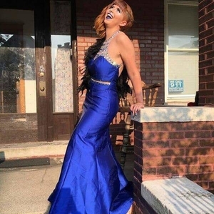 Photo of Gigi Bella. She is wearing a dark blue dress with a rhinestone neckline. She is throwing her head back and smiling widely.