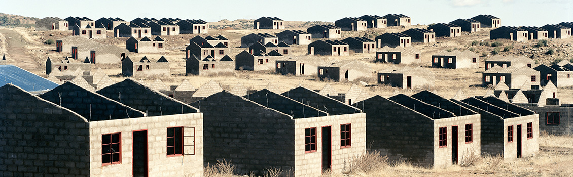 Photo of concrete block buildings without roofs, windows have no panes and red lintels.