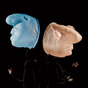 Two dancers in black so that their bodies can't really be seen with blue and peach masks that look air filled.  The noses are prominent and facing out.