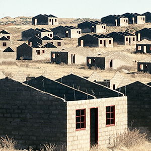 Photo of concrete block buildings without roofs, windows have no panes and red lintels.