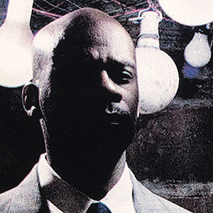 Poto of a man's head in front of light bulbs.  There is a grainy quality and some highlights in pink and blue.  The lower half of the man's face is in shadow.