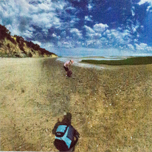 A photo of a person in the mid ground and a blue bag in the front.  The sky has puffy small clouds.  The whole photo looks posterized and a little grainy.