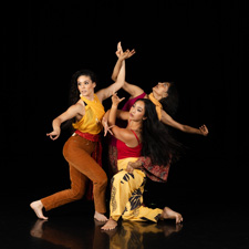 Three female dancers wearing colorful clothing and posing.