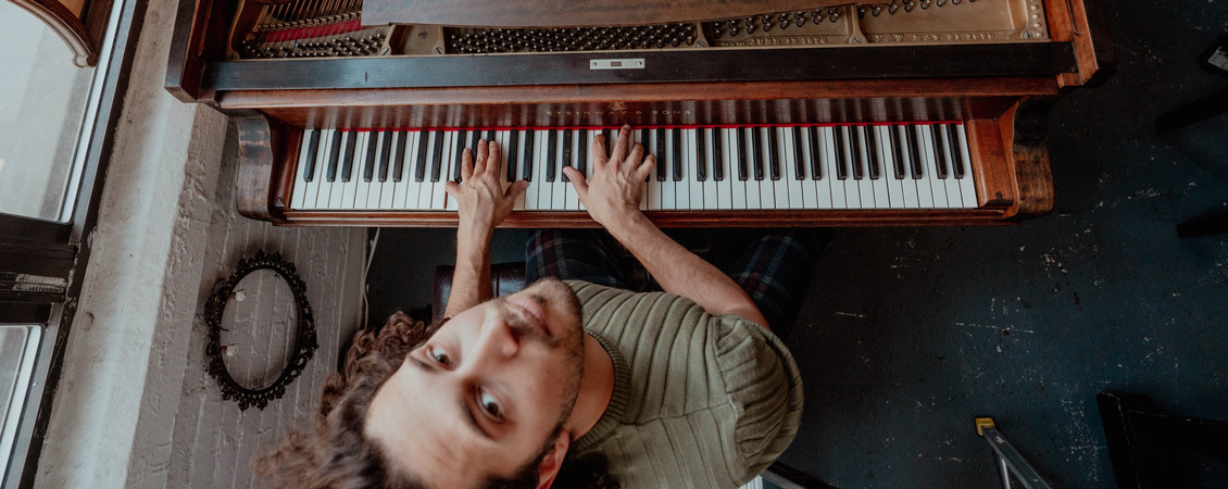 A bird's-eye view of Emmet playing the piano. He is looking up at the camera 