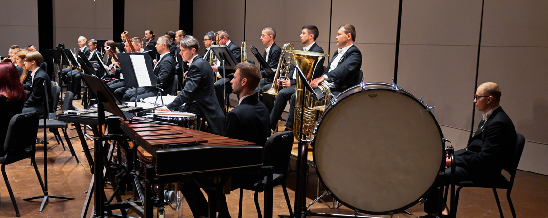 Photo of a part of an orchestra. Closest to the camera are drums and xylophone. There are also people with trombones visible in the background 