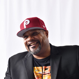 An African American man in a black suit and a red hat with a P on it.