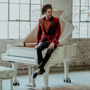 A photo of Emmet in a red suit sitting on top of a white grand piano looking to the left