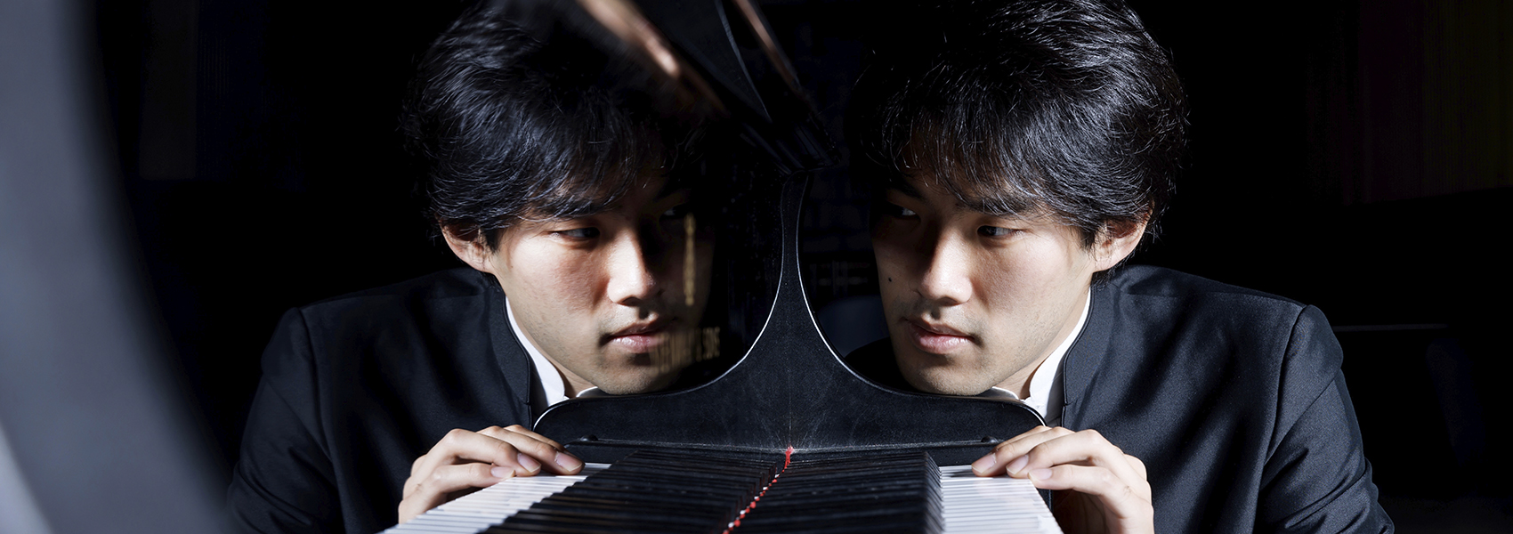 Pianist Bruce Liu is pictured with his chin resting on a piano.