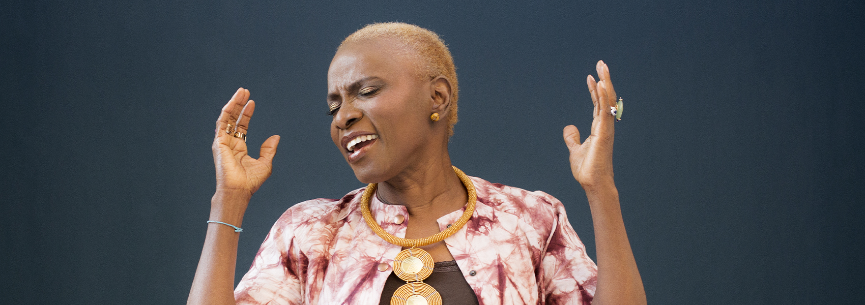 Angelique Kidjo is pictures singing with her eyes closed and her hands raised in the air. 