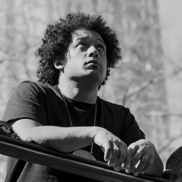 Makaya McCraven is pictured standing on a bridge with his hands on the railing in a black and white photograph.