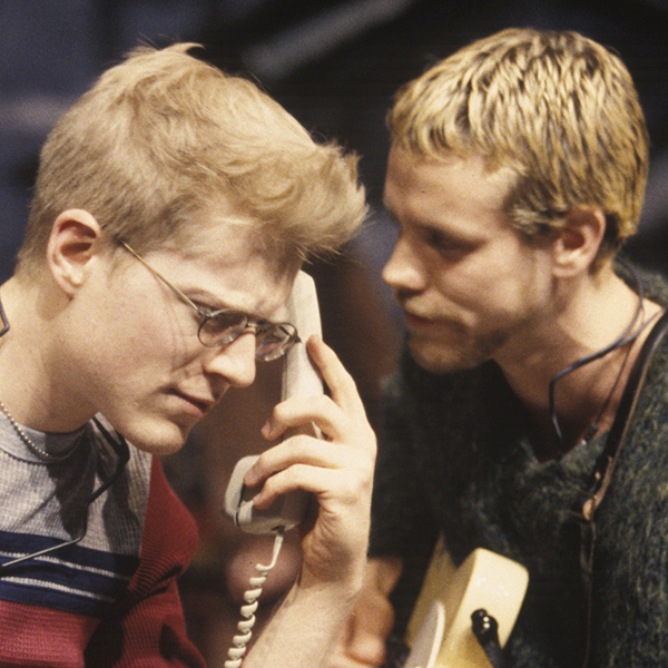 Anthony Rapp and Adam Pascal are pictured seated onstage in a performance of RENT.