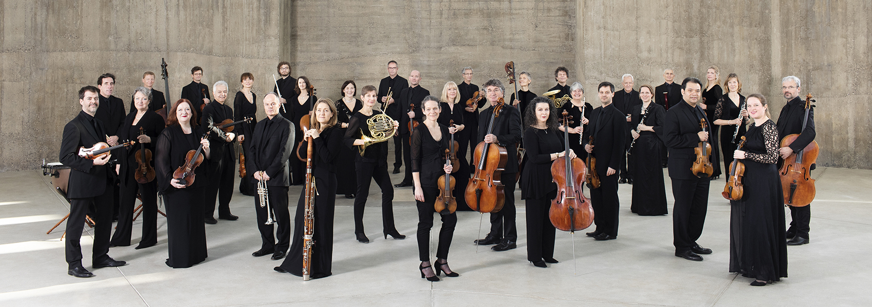 Academy of St Martin in the Fields musicians stand in a group dressed in black and holding their instruments